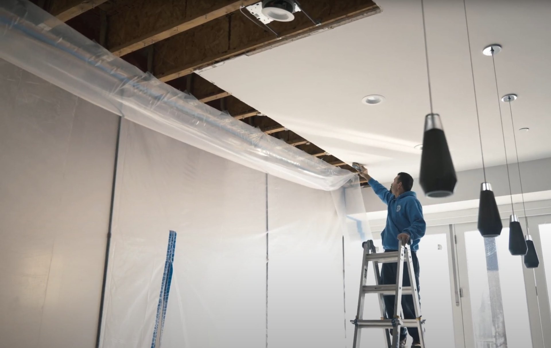 Water damage restoration professional working on ceiling repair with protective equipment